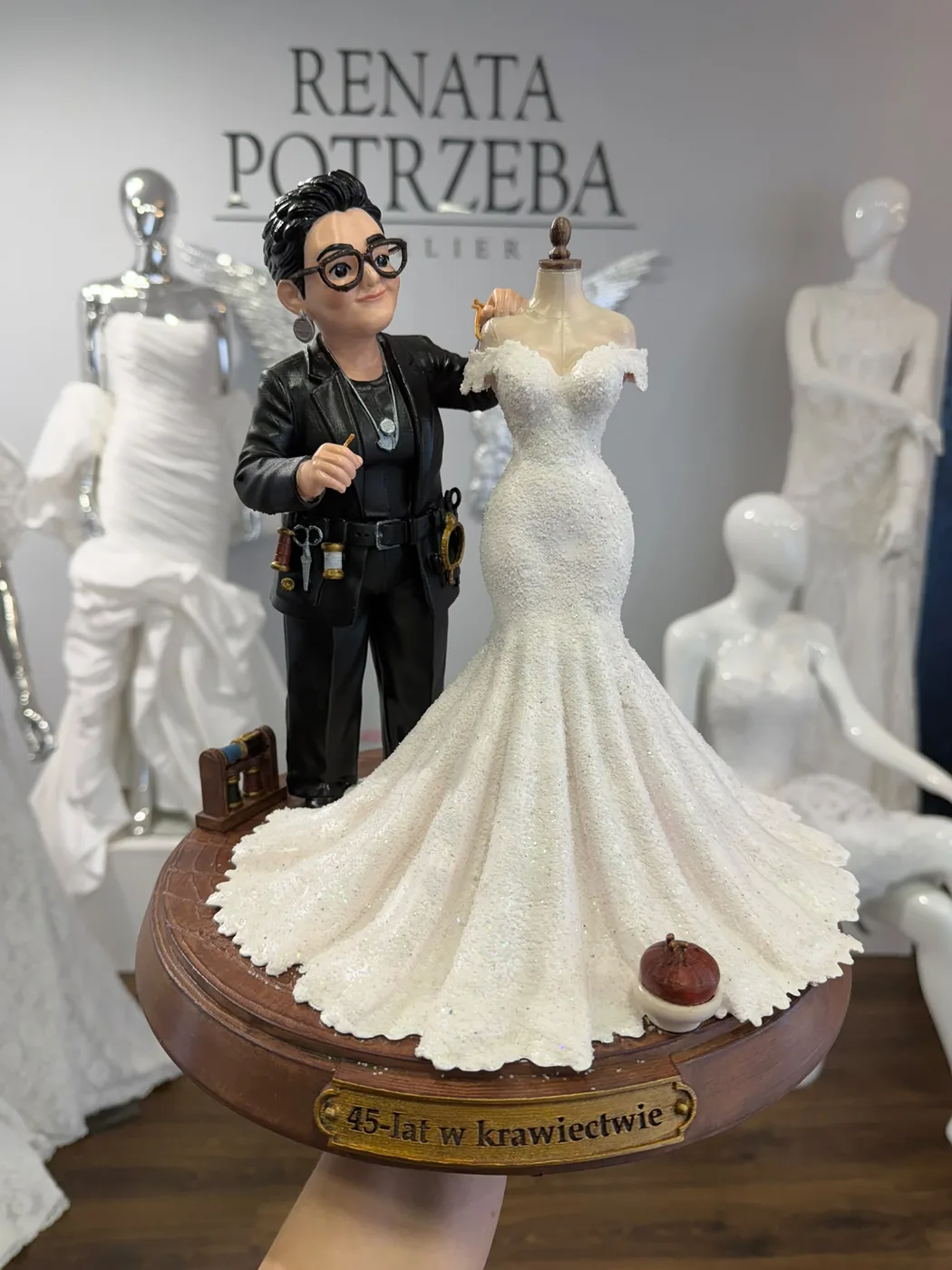 Kreskówkowa figurka krawca obok manekina w białej sukni ślubnej, na brązowej podstawie ze złotą tabliczką - druk 3D