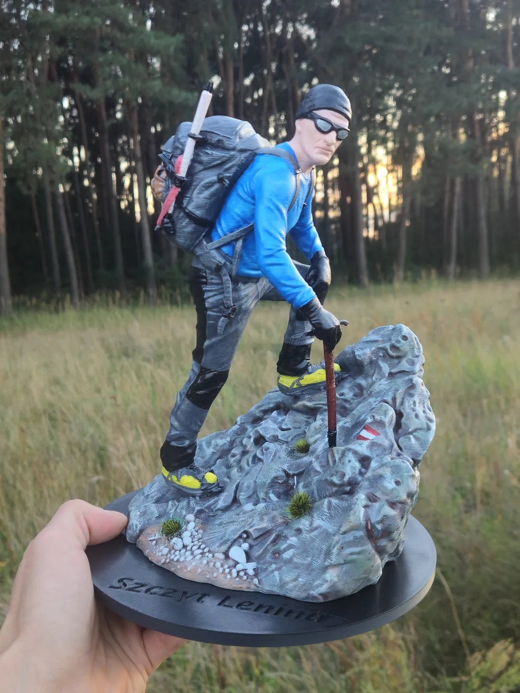 Figurka zdobywcy szczytów trzymana w dłoni, na tle łąki i lasu - druk 3D